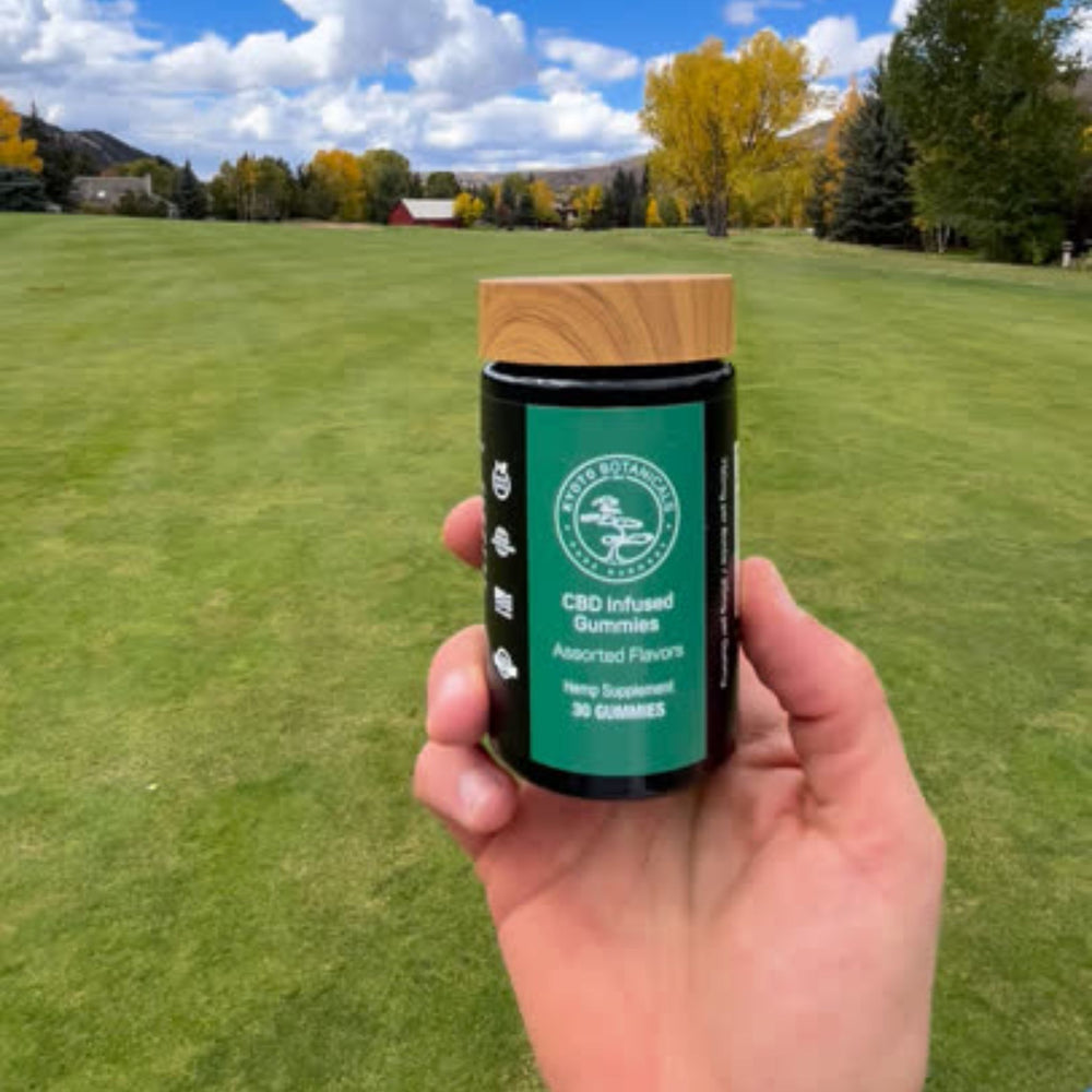 Hand holding a CBD-infused gummies container with a golf course background