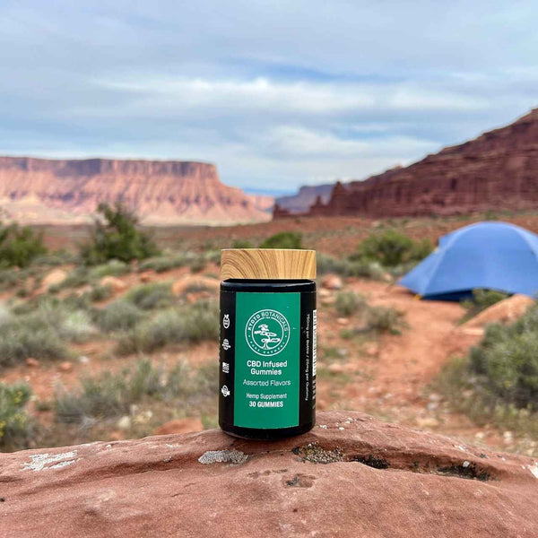 CBD-infused gummies jar on a rock with desert landscape and blue tent in the background