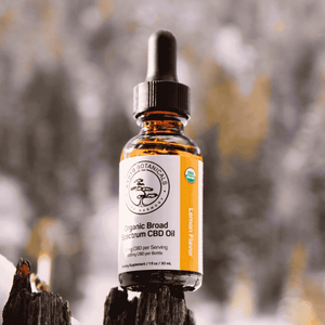 Kyoto Botanicals Organic Lemon CBD Oil bottle standing on wood with snowy mountain background — USDA Certified Organic broad-spectrum hemp tincture.