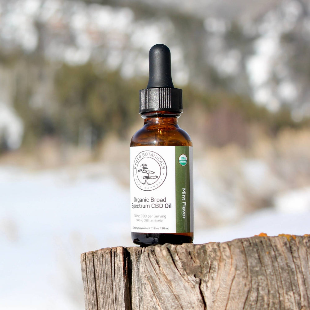 organic CBD oil bottle with dropper on a wooden log against a snowy forest background